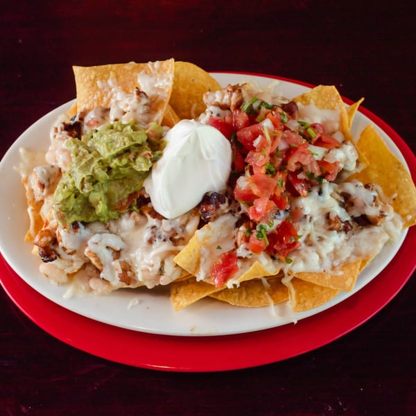 A plate of cheesy nachos topped with guacamole, sour cream, and pico de gallo.