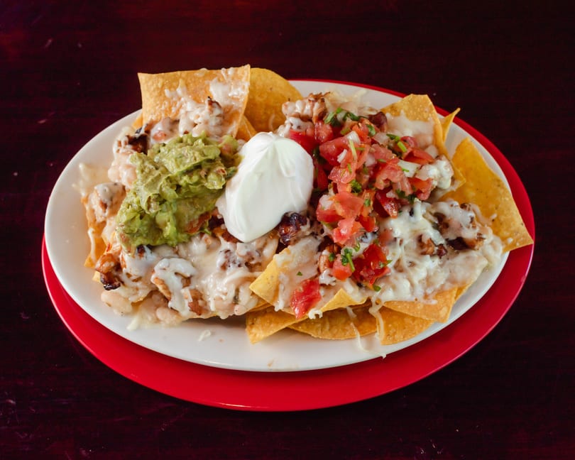 A plate of cheesy nachos topped with guacamole, sour cream, and pico de gallo.