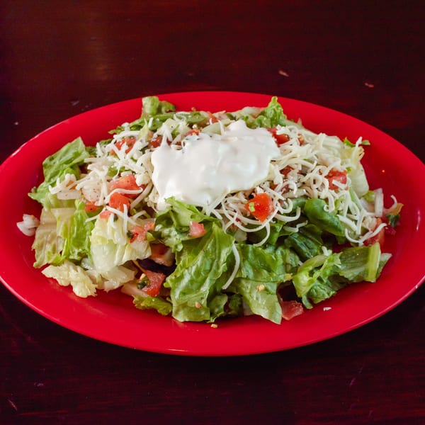 A vibrant red plate holds a fresh salad topped with shredded cheese, diced tomatoes, and a dollop of sour cream.