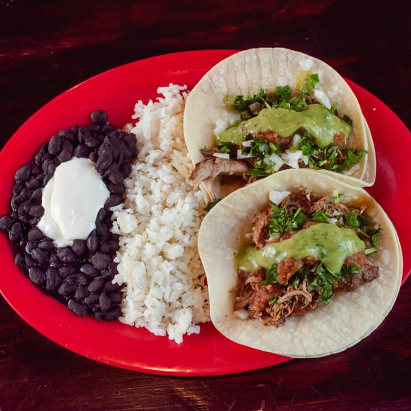 Two tacos with meat, cilantro, onions, and green sauce, served with rice and black beans.
