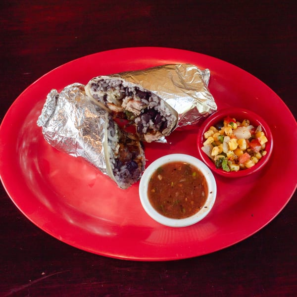 Two foil-wrapped burritos, salsa, and corn salad on a red plate.