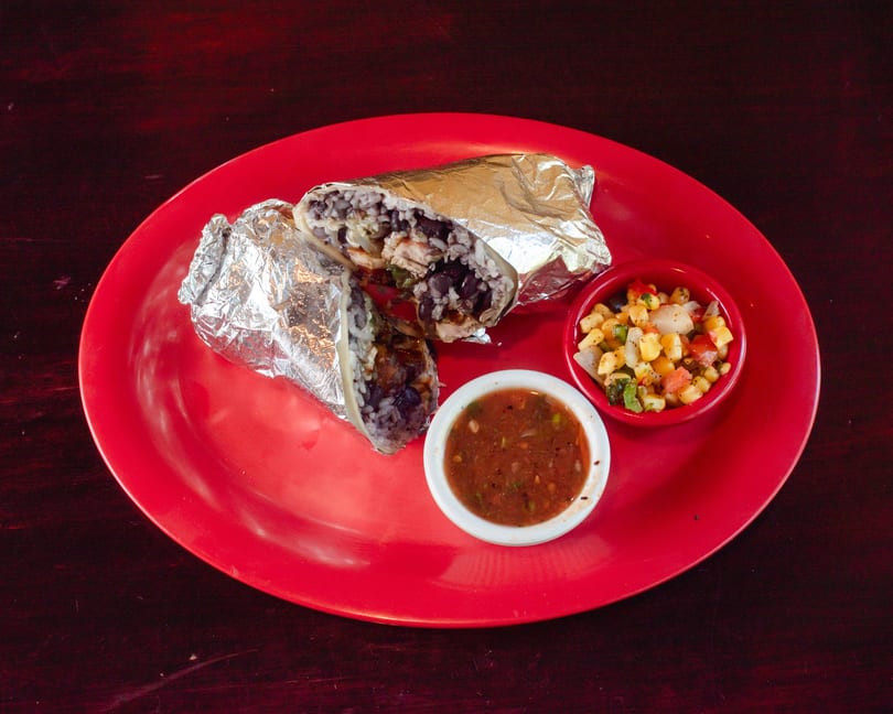 Two foil-wrapped burritos, salsa, and corn salad on a red plate.