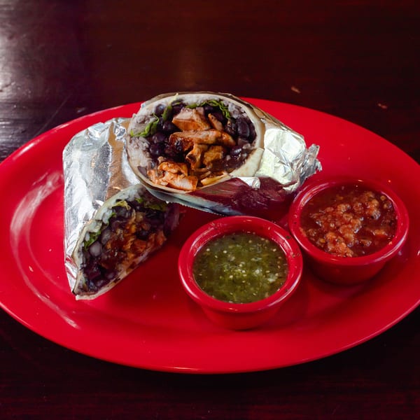Two foil-wrapped burritos, one cut open, filled with chicken, black beans, and rice, served with two salsas on a red plate.